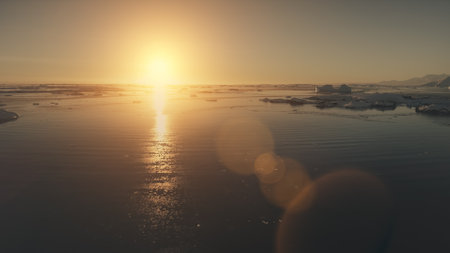 Antarctica sunset. Epic aerial view drone flight. Fast time lapse shot over the ocean water and glacier ice. Orange sun light given bright beams. 4k footage.の写真素材