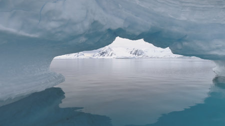 Antarctica Shot Through Iceberg Arch. Snow Covered Mountains Background. Amazing View Of Mighty...