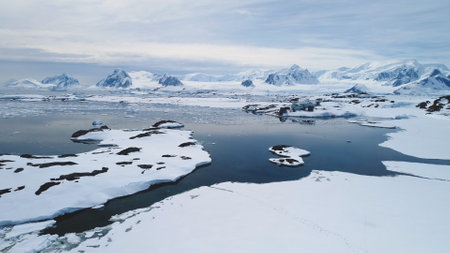 Aerial Flight over Antarctica Vernadsky Base, Snow Shoreline and Ocean. Drone Overview of Polar Surface and Ice Frozen Ocean. Snow Covered Mighty Mountains Background in Antarctic Land. 4k Footage.の写真素材