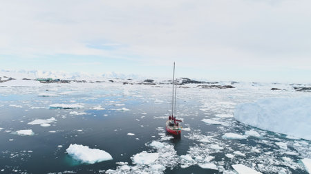 Sailing Yacht Travel in Antarctica Calm Brash Ice Ocean among Iceberg Aerial Tracking Shot. Red Boat...