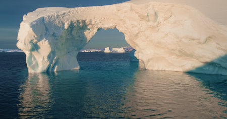 Drone flight into big glacier arch in Antarctica. Huge hole in melting iceberg, ocean water, polar...