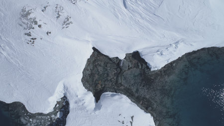 Aerial view to Antarctic ocean surface and snow-covered islands. Camera looks down, slowly rises to...