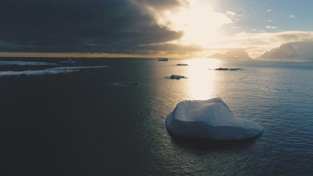 Iceberg in sunset above Antarctica. Front aerial view. Sun reflection on ocean water in Antarctic summer. Beautiful ice, sky and ocean landscape. Drone forward flightの写真素材