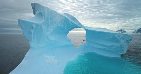 Giant blue melting iceberg with cave drifts ocean water. Drone fly inside ice glacier hole. Polar...