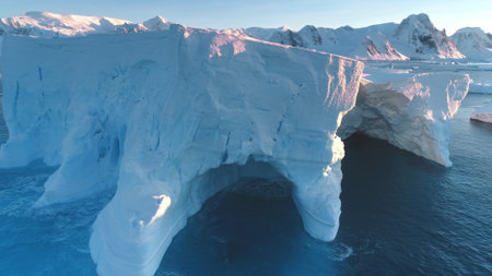 Huge iceberg towering in sunset light in Antarctica. Melting glacier holes and caves washed by ocean...