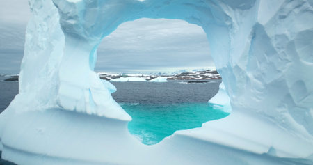 Huge hole in melting iceberg in Antarctic ocean close up. Flight inside frozen glacier cave arch window drifting blue cold water. Arctic winter landscape, global warming problem. Polar climate changeの写真素材