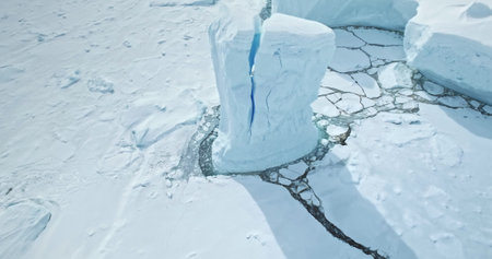 Aerial view cracked blue iceberg towering in Antarctica ocean. Calving snow covered glacier on South...