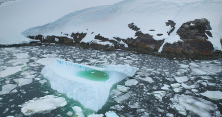 Zoom in large melting iceberg with green lake inside drifting in Antarctica. Cold ice floes polar...