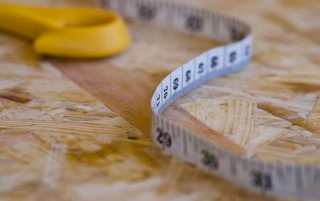 Measuring tape isolated on a wooden  background with yellow scissor