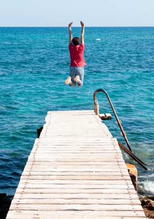 Young woman jumping from the pier to the sea の写真素材