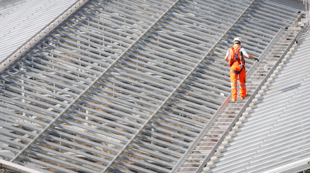 Male Worker wearing an orange suit walking on the top of a steel roof structure of a railway stationの写真素材