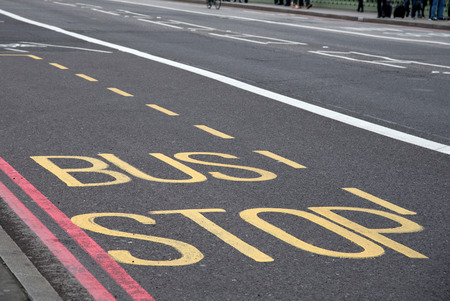 Bus stop information sign written on a  bus lane on an empty  street.