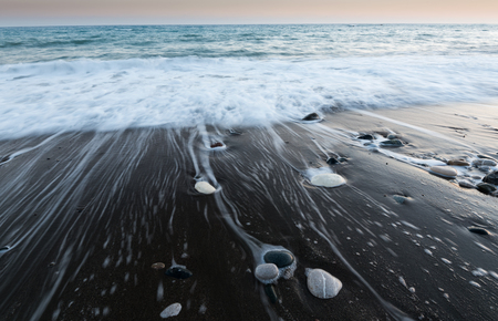 Pebbles on  the beach on a black sand and flowing sea water creating nice textures. Long exposure image.の写真素材