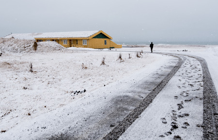 Unrecognized man walking on a snowy road to the yellow winter cottage house in Icelandの写真素材