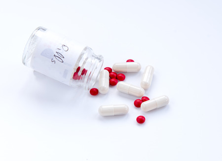 Bottle with white medical capsules and red pills.の写真素材