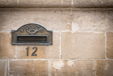 Old bronze metal letter box and house number on bricked wall