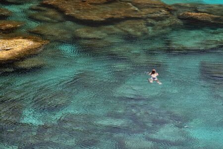 Young unrecognised woman swimming at the deep blue clean and calm sea waters near the sea cave at...