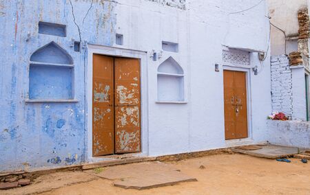 Traditional exterior of an Indian house with blue wall and red closed doors at the village of...