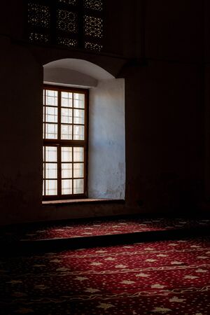 Closed glass church window with sunlight entering and brightening the interior carpet floor of the...