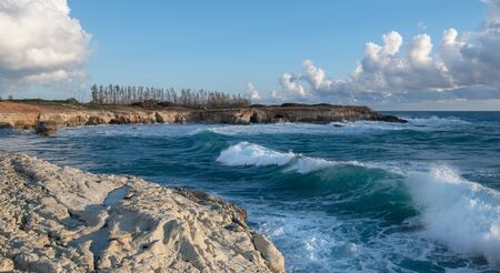 Sea waves splashing on the rocks of a rocky beach against blue cloudy sky. Paphos Cyprusの写真素材
