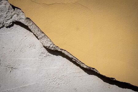 Old cracked and dangerous collapsing yellow wall of an abandoned house