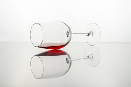 Glass of red wine resting and reflected on a transparent white surfaceの写真素材