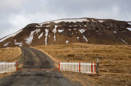 Wooden entrance open gate, empty road and snowy mountain in Icelandの写真素材