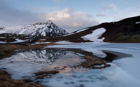 Typical Icelandic dramatic landscape with frozen lake and mountains covered in snow at snaefellsnes peninsula in Icelandの写真素材