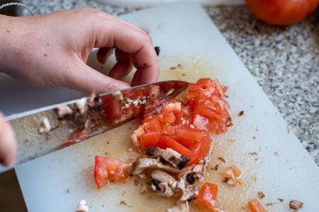 Knife cutting tomatoes and mushrooms on pieces on a cutting board. Preparing foodの写真素材