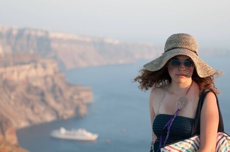 Beautiful happy girl wearing a hat with caldera view behind in Santorini Island in Greece. Summer vacations in Greek Islandsの写真素材