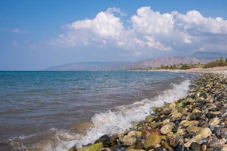 Sea waves splashing to a pebble rocky beach against cloudy skyの写真素材