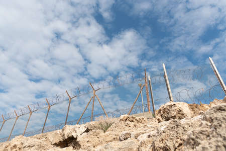 Security fence with barbed wire against a blue cloudy skyの写真素材