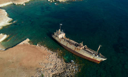 Aerial drone view of an abandoned ship moored at the coastal rocky area.