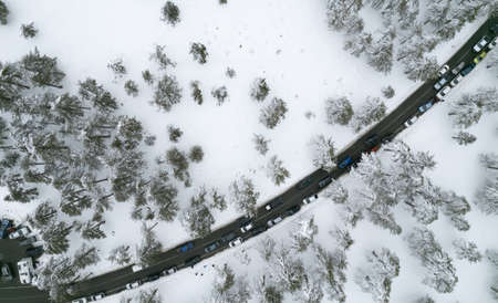 Drone aerial of a car parking on the snowy forest mountain in winter.