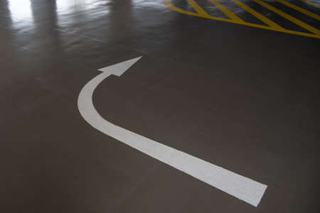 White arrow directive sign on a car parking lot. Direction sign, safe exit parking