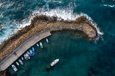Aerial drone view of fishing boats moored at harbor at breakwater. Stormy waves at seaの写真素材