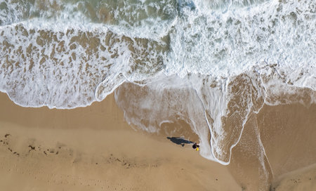 Aerial drone point of view of pernon walking on sand in a beach. Stormy waves idyllic beach in...