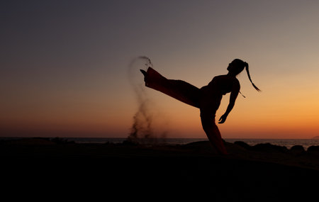 Silhouette of a woman dancing at a sandy beach at sunset. Caucasian woman posing outdoors at the coastの写真素材