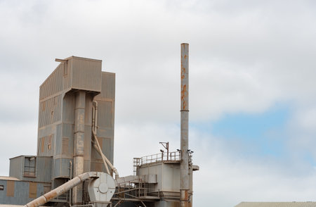 Metallic industrial factory building with chimneys against cloudy sky. Environmental pollution. Heavy industryの写真素材