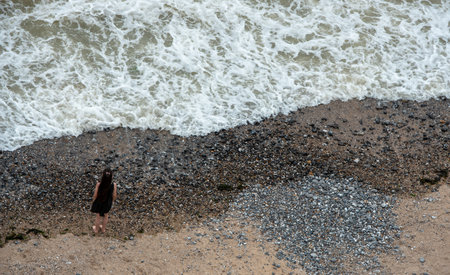 young girl in standing in the beach and looking at the stormy spindrift waves.の写真素材