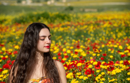 Portrait of a young woman dressed in red smiling in the field of red poppies in spring. Springtime blooming seasonの写真素材