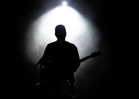 Musician playing guitar performing on stage under spot light. Silhouette of a music artist and band on stageの写真素材
