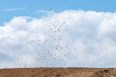 Debris fly after motocross roaring against cloudy sky.