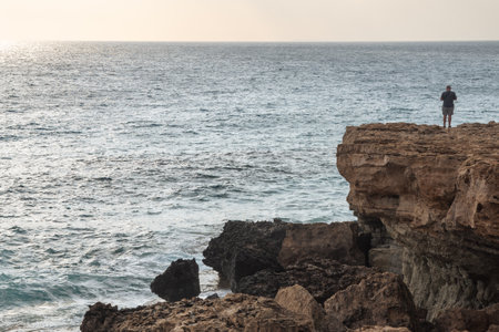 Unrecognized person standing at the edge of rocky coast sightseeing enjoying sunset