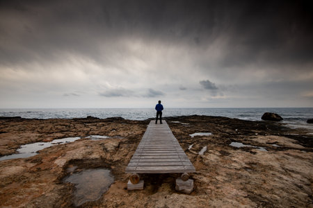 Man standing alone at the edge of rocky beach in Stormy Weather