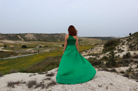 Young woman wearing long green dress standing at the edge of a cliff enjoying the spring scenery. Female person active outdoorの写真素材