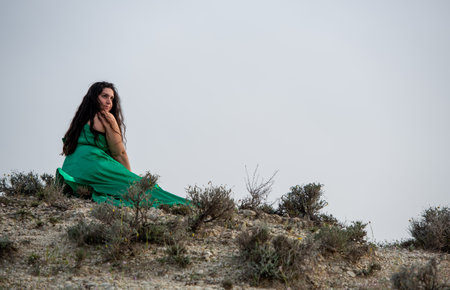 Young woman wearing long green dress sitting at the edge of a cliff enjoying the spring scenery. Female person active outdoor. Copy spaceの写真素材