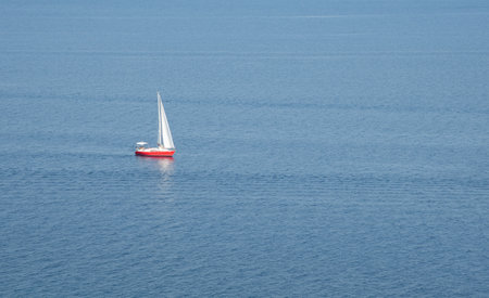 White sailboat sailing on calm blue sea from island clifftopの写真素材