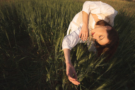 Young woman wearing white dress relaxing in wheat fieldの写真素材