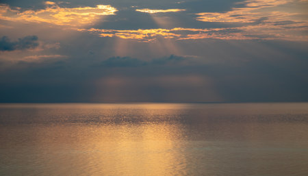 Sun shining through clouds over calm ocean at sunrise